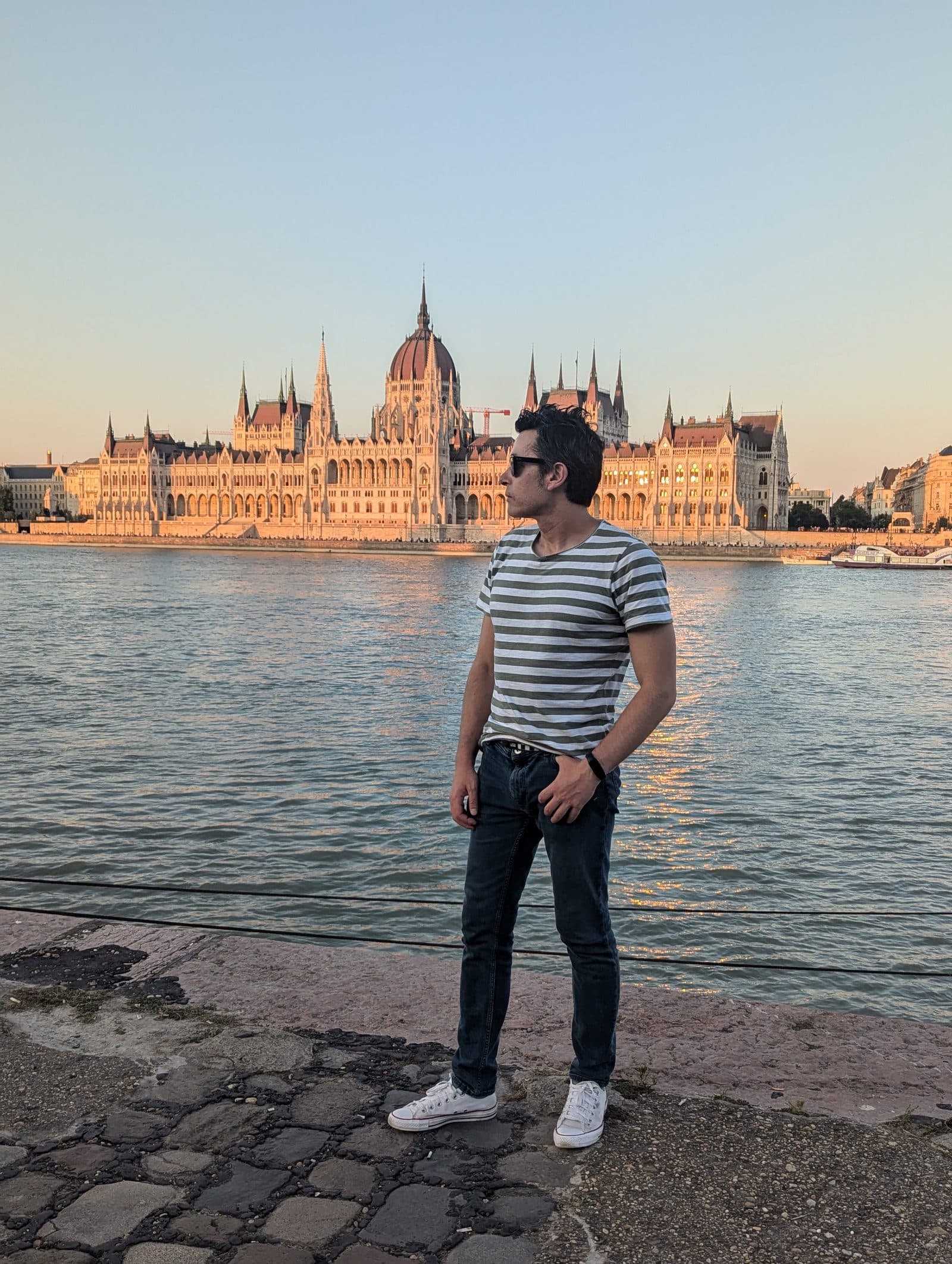 Diego Fresno standing on the Danube embankment in Budapest, with the Hungarian Parliament building lit by low sun behind him